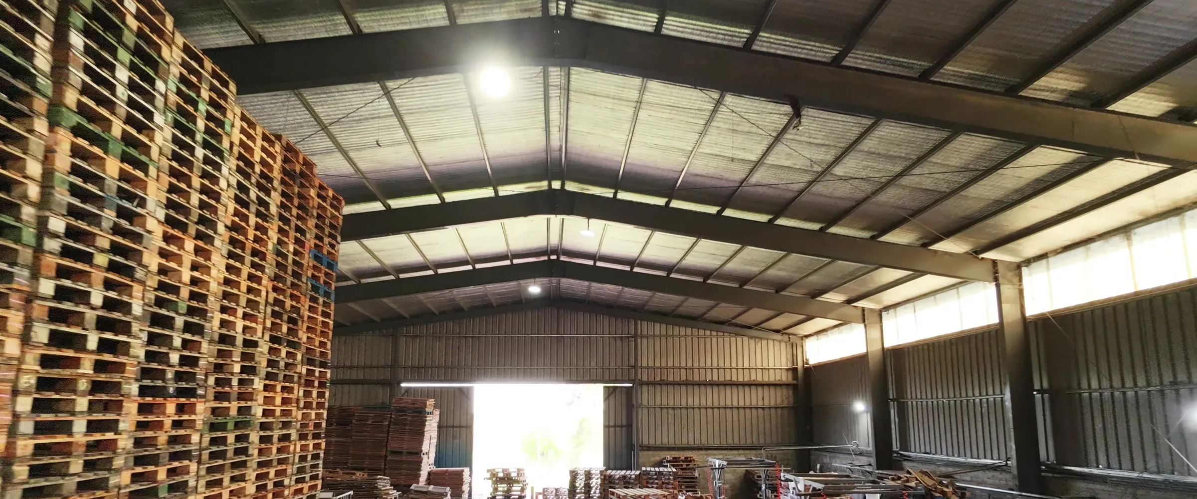 Nave de Transpallets con una pared de pallets apilados en altura, el techo de estructura metálica y el portón al fondo